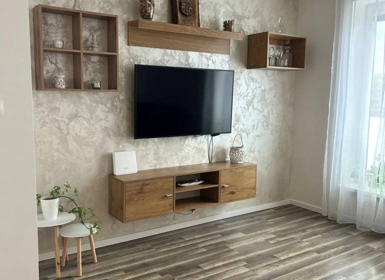 Obývací pokoj v 3-pokojovém bytě s podlahou s dřevěným dekorem, zavěšenou TV a dekoracemi.