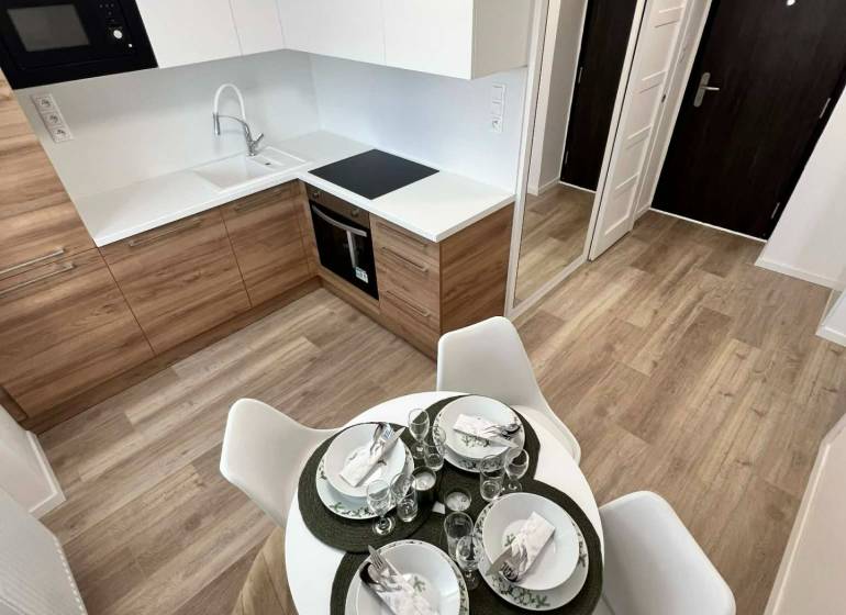Kuchyně v 2pokojovém bytě s podlahou s dřevěným dekorem a jídelním stolem.