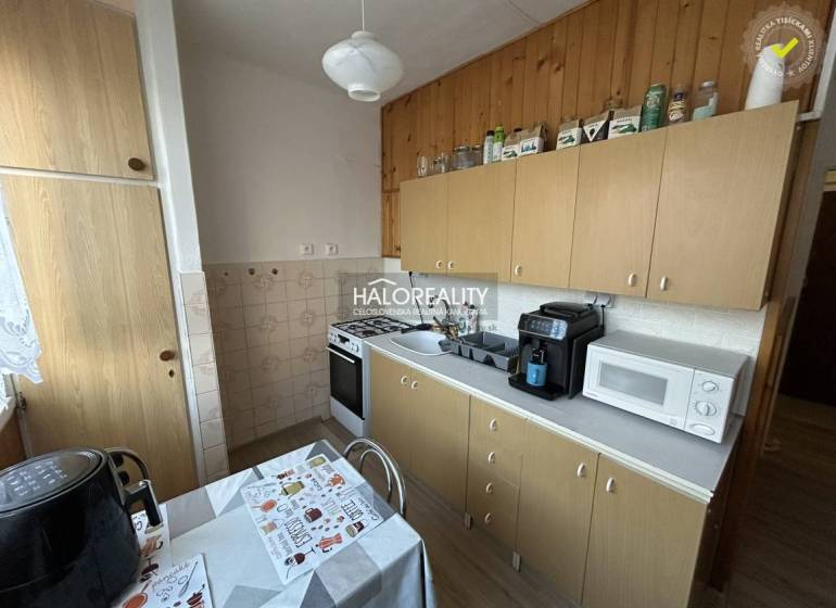 Kuchyně v 2-pokojovém bytě s dřevěným dekorem, včetně spotřebičů a jídelního stolu.