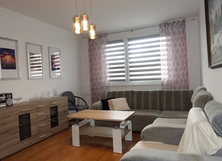 Světlý obývací pokoj s rohovou sedačkou, stolkem a komodou ve 3pokojovém bytě.