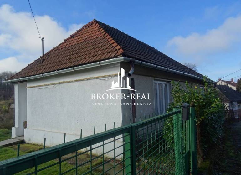 Rodinný dům v Rudabányi s bílou fasádou a šikmou střechou za zeleným plotem.