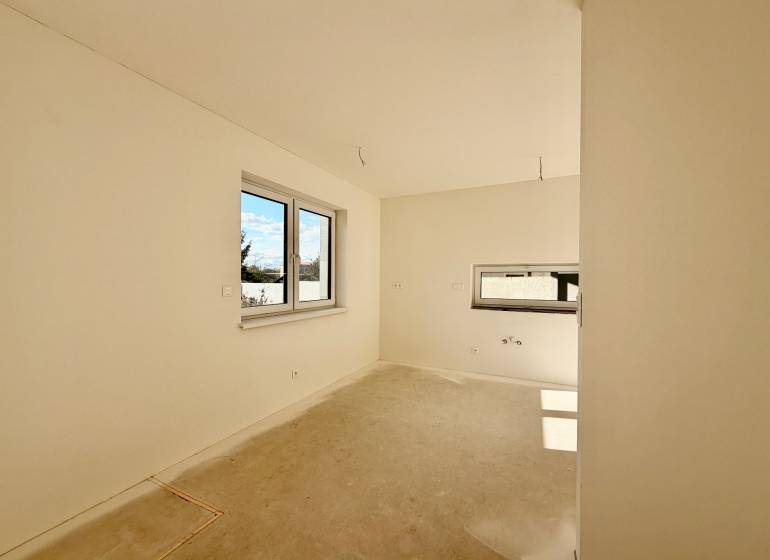 Prázdný pokoj s dvojitým oknem a betonovou podlahou v rodinném domě.