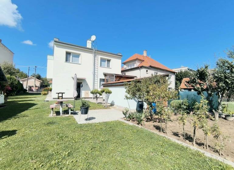 Rodinný dům v Partizánském obklopený zeleným trávníkem a zahradou pod modrou oblohou.