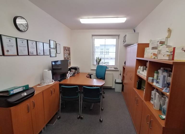 Kanceláře s nábytkem, certifikáty na stěně a policemi s produkty.