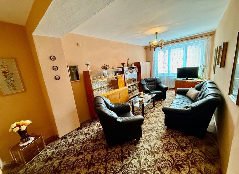 Obývací pokoj v 2-pokojovém bytě s pohovkou a prosklenou vitrínou.