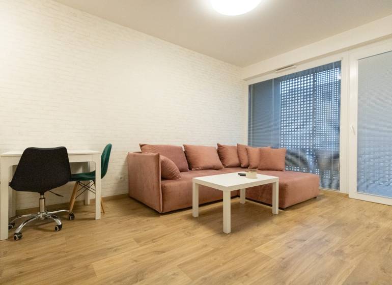 Obývací pokoj v 2pokojovém bytě s pohovkou, stolem a podlahou s dřevěným dekorem.