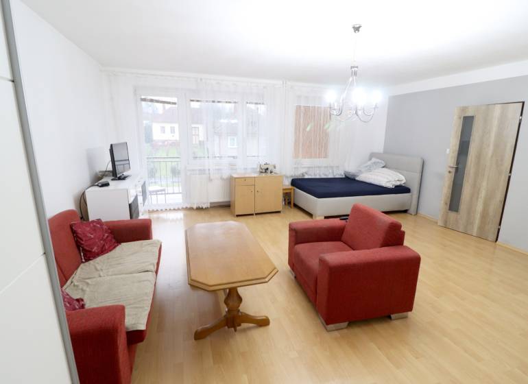 Obývací pokoj v rodinném domě s pohovkou, stolem a postelí. Podlaha s dřevěným dekorem.