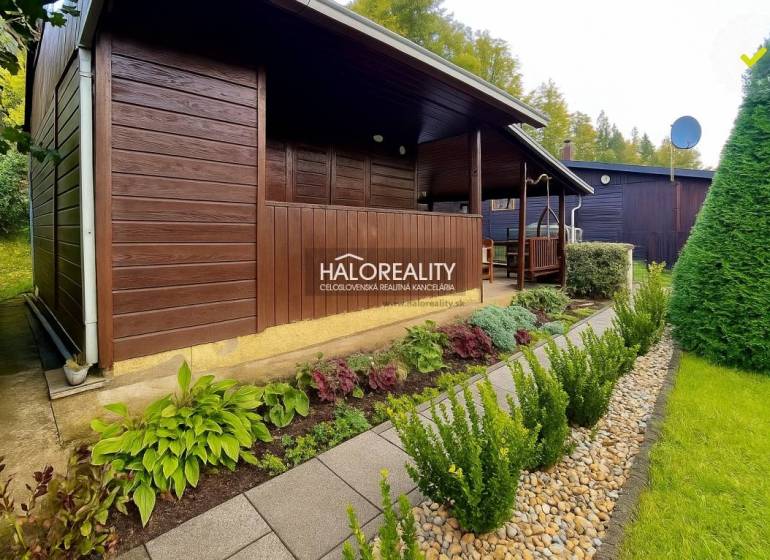 Dřevěná chatka v zahradách v Bytči, obklopená udržovanou zelení a chodníkem z dlaždic.