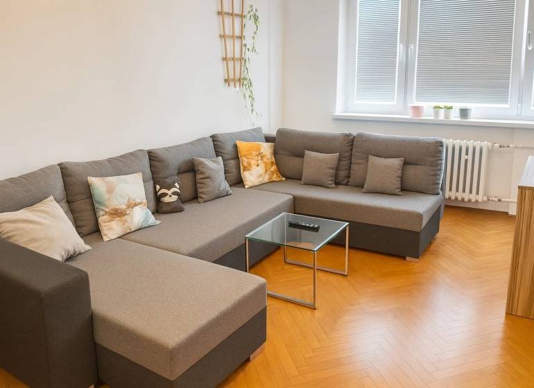 Obývací pokoj s pohodlnou sedačkou a podlahou s dřevěným dekorem v 3-pokojovém bytě.