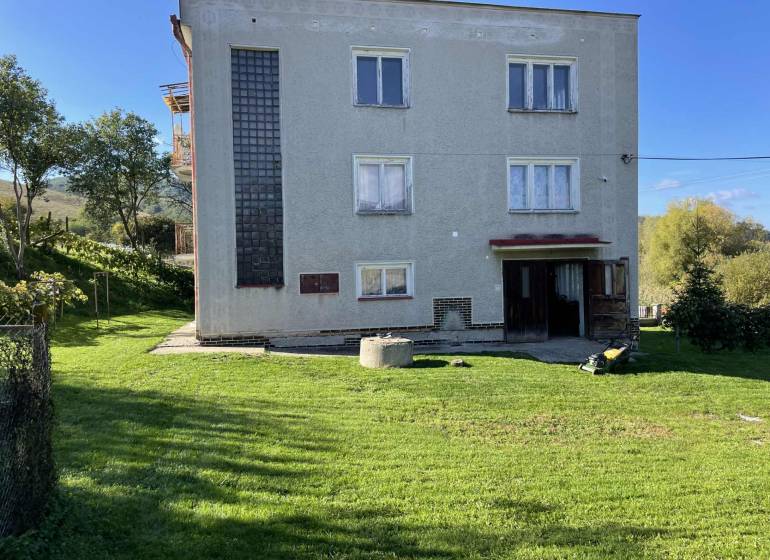 Rodinný dům v Hajnáčce s trávníkem, stromy a zahradním nářadím na dvoře.