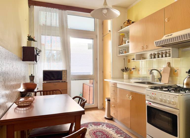 Kuchyňa v 2-izbovom byte s dreveným dekorom podlahy, stolom a kobercom.