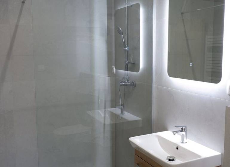 Koupelna s umyvadlem, sprchovým koutem a velkým zrcadlem v rodinném domě.