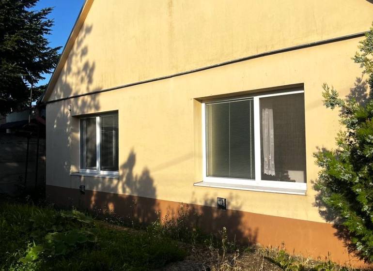 Rodinný dům v Diakovcích se šikmou střechou a žlutou fasádou, obklopený zelení.