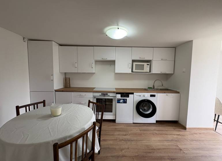 Kuchyně v 1-pokojovém bytě s bílými skříňkami a podlahou s dřevěným dekorem.