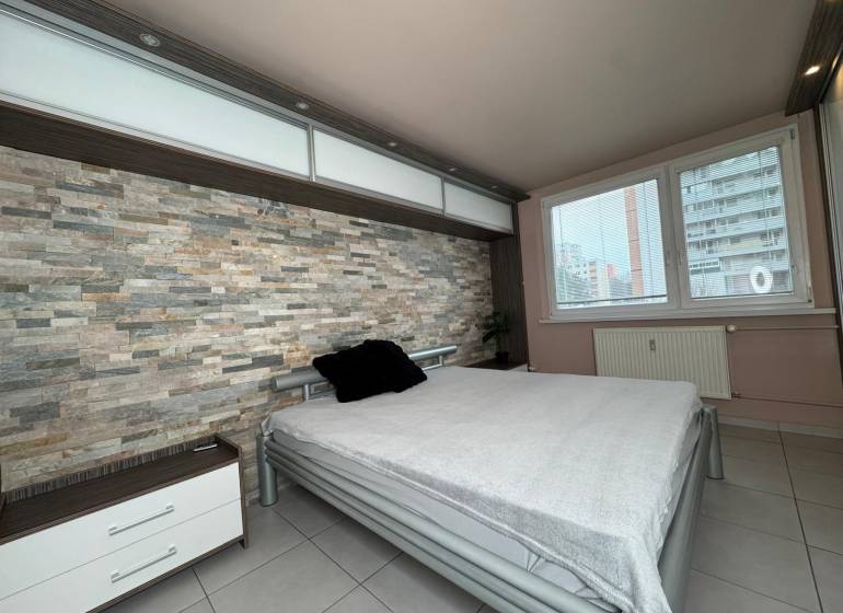 Ložnice s kamennou stěnou a velkým oknem v 3-pokojovém bytě.