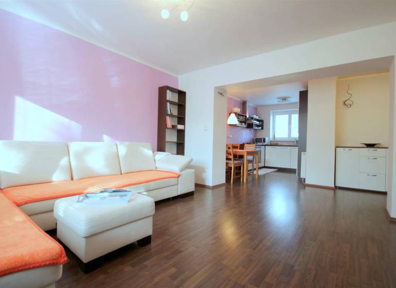 Obývací pokoj v 2-pokojovém bytě s rohovou sedačkou a podlahou s dřevěným dekorem.