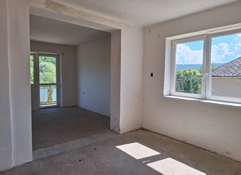 Pokoj v rodinném domě, velká okna, výhled na zahradu a okolní stromy.