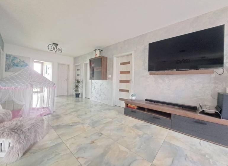 Obývací pokoj v rodinném domě s televizí na stěně, stanem a keramickou podlahou.