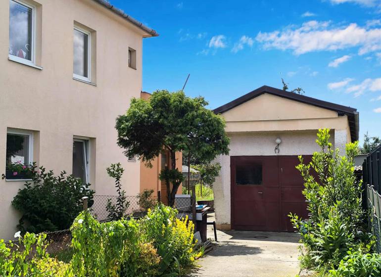 Rodinný dům v Partizánskem s garáží obklopený zahradou plnou zelených rostlin.