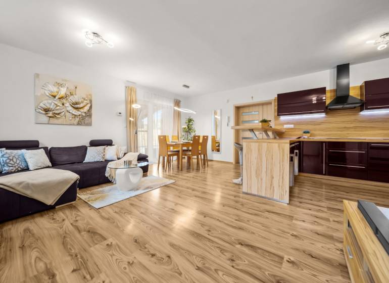 Obývací pokoj a kuchyňa v rodinném domě s podlahou s dřevěným dekorem, pohodlný gauč.