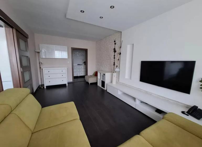 Obývací pokoj v 3pokojovém bytě s podlahou s dřevěným dekorem, TV a sedací soupravou.