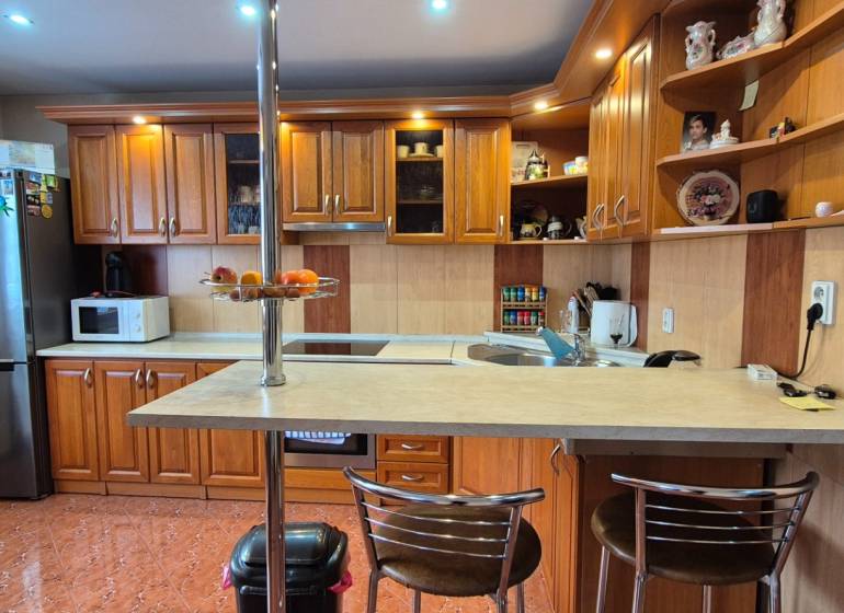 Kuchyně v rodinném domě s dřevěnými skříňkami, barovým pultem a spotřebiči.