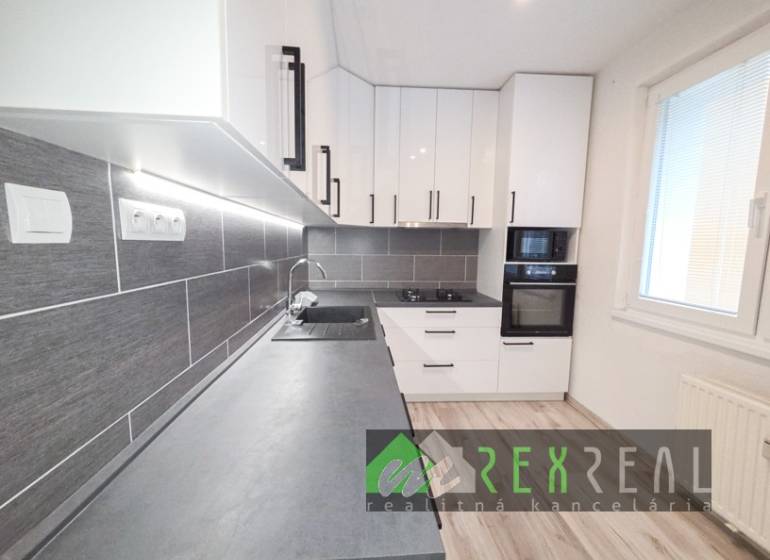 Kuchyně ve 3-pokojovém bytě s bílými skříňkami, šedou pracovní deskou a podlahou s dřevěným dekorem.