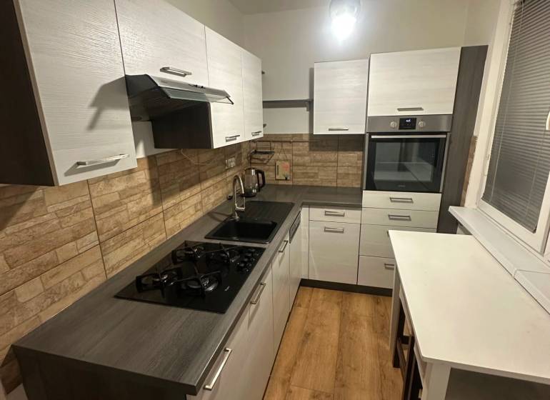 Kuchyně v 2-pokojovém bytě s podlahou s dřevěným dekorem a stěnami z cihel.