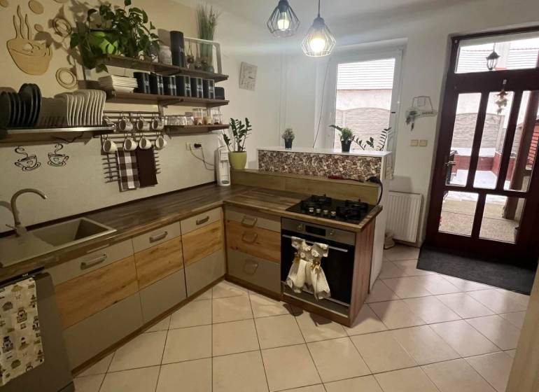 Kuchyně v rodinném domě s keramickou dlažbou, dřevěnými dekoracemi a otevřenými policemi.