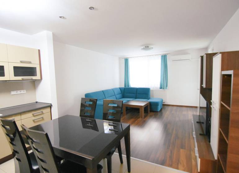 Obývací pokoj s modrou sedačkou, kuchyní a podlahou s dřevěným dekorem v 2-pokojovém bytě.