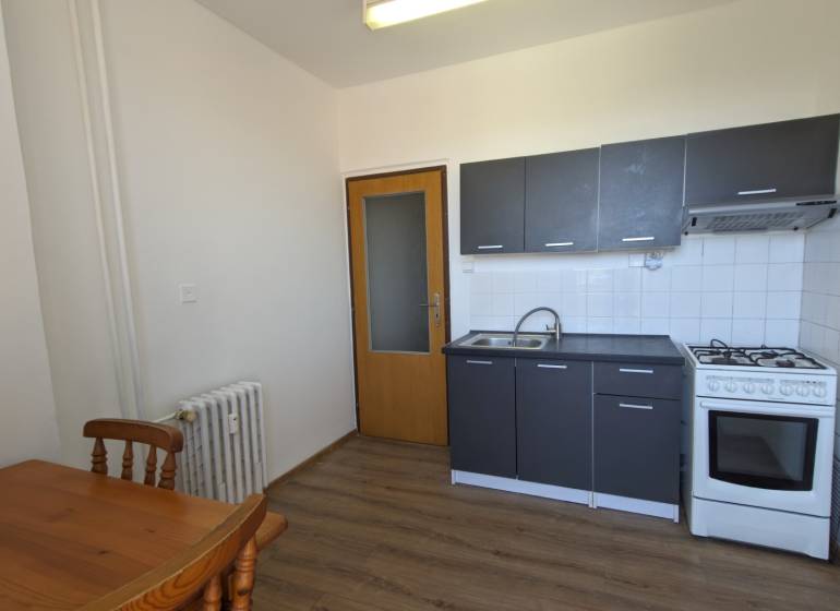 Kuchyně s šedou linkou a dřevěným stolem v 1-pokojovém bytě, podlaha s dřevěným dekorem.