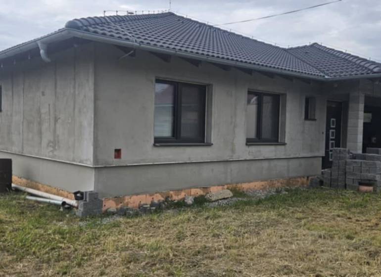 Rodinný dům z neomítnutých zdí v Semerově s šindelovou střechou na travnatém pozemku.