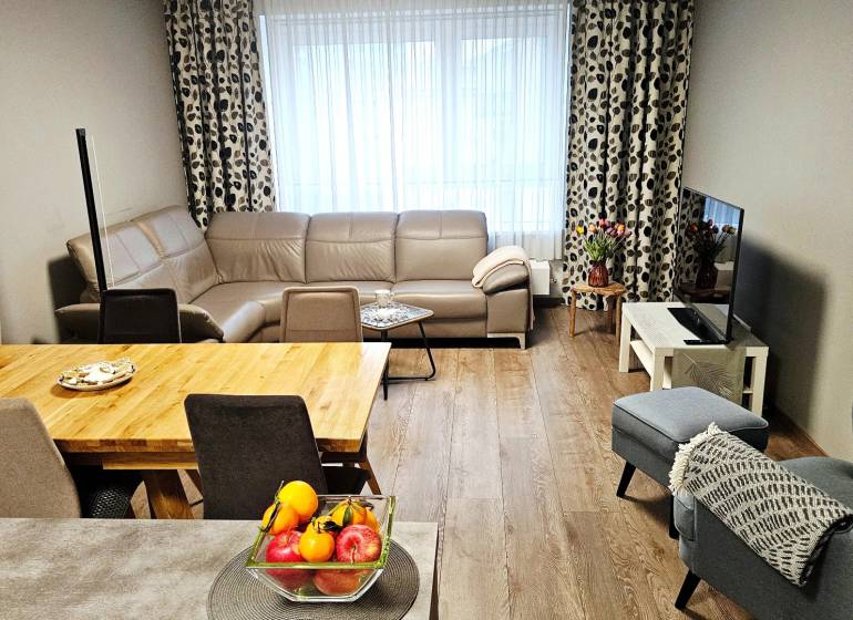 Obývací pokoj v 3-pokojovém bytě s koženou sedačkou a podlahou s dřevěným dekorem.