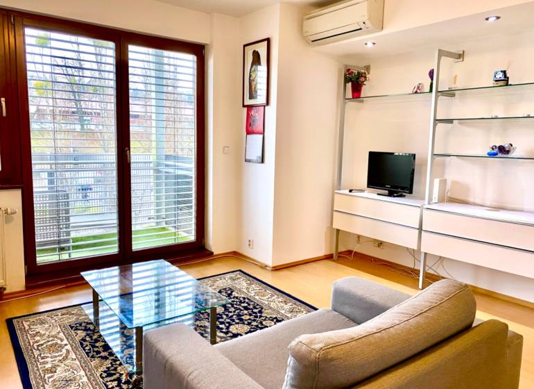 Obývací pokoj v 2-pokojovém bytě s křeslem, skleněným stolem a podlahou s dřevěným dekorem.