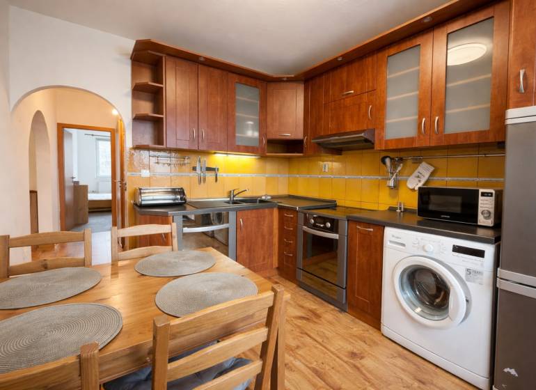 Kuchyně 4pokojového bytu s dřevěným dekorem, vybavená spotřebiči, jídelní stůl, žluté obklady.