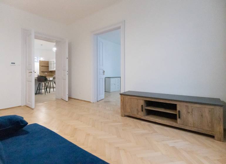 Obývací pokoj 3pokojového bytu s modrou sedačkou a podlahou s dřevěným dekorem.