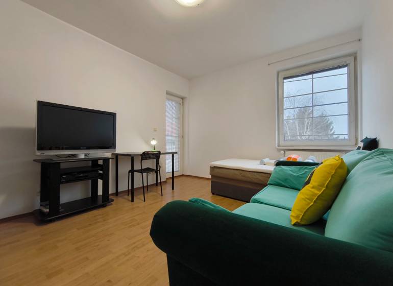 Obývací pokoj v rodinném domě s pohovkou, televizí, stolkem a podlahou s dřevěným dekorem.