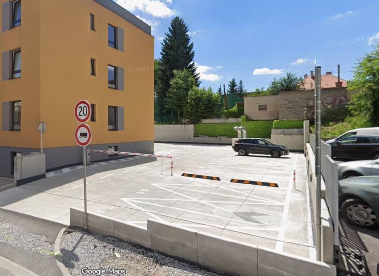 Parkoviště a obytná budova na Rudlovské cestě v Banské Bystrici obklopené zelení.