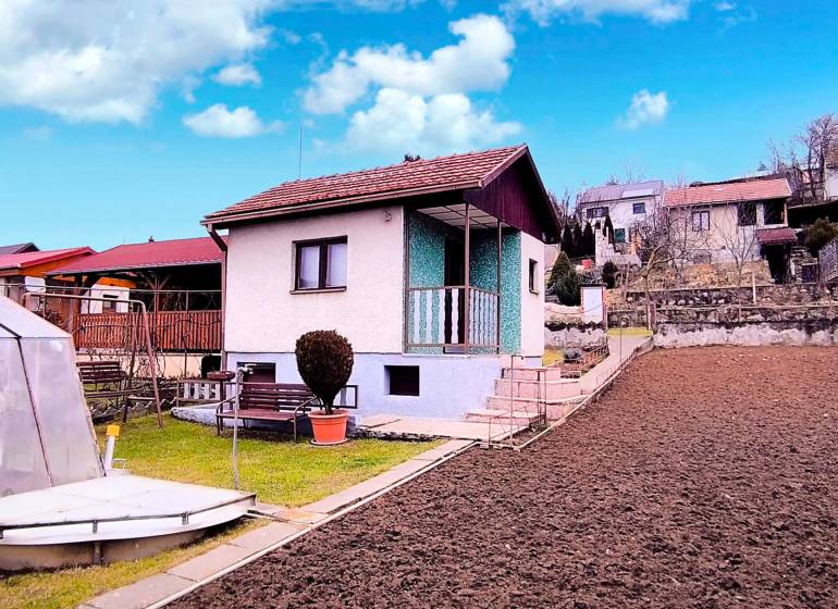 Chata v Partizánskych s jednoduchou zahrádkou, obrubníky a altánkem pod modrou oblohou.