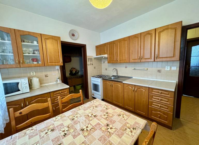 Kuchyně s dřevěnými skříňkami a jídelním stolem, vhodná pro 3pokojový byt.