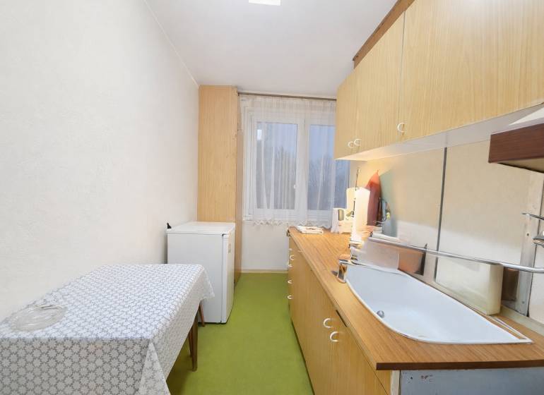 Kuchyně ve 3-pokojovém bytě s jednoduchým zařízením, podlaha s dřevěným dekorem.