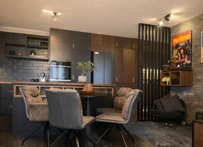 Kuchyně v 2-pokojovém bytě s tmavými skříňkami a dekorativními plakáty na stěně.