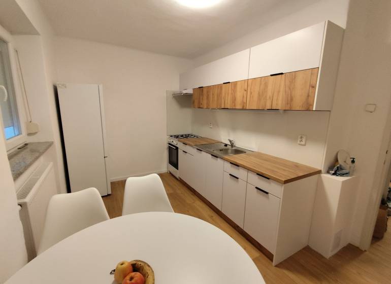 Kuchyně v 2-pokojovém bytě se světlými skříňkami a podlahou s dřevěným dekorem.