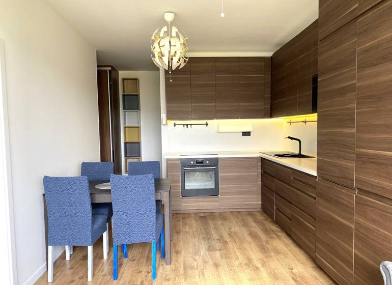 Kuchyně v 3-pokojovém bytě s jídelním stolem, moderním osvětlením a podlahou s dřevěným dekorem.