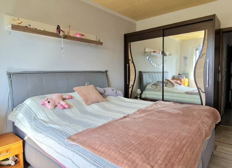 Ložnice v dvoupokojovém bytě se zrcadlovou skříní a čalouněnou postelí.