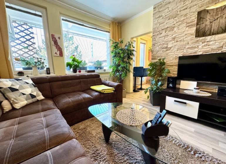 Obývací pokoj v 1-pokojovém bytě s hnědou sedačkou a podlahou s dřevěným dekorem.