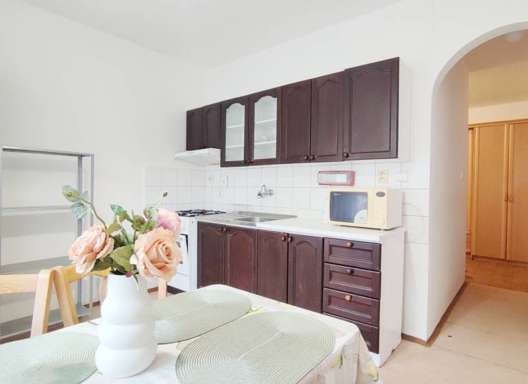 Kuchyně v 2-pokojovém bytě s tmavými skříňkami a jídelním stolem s dekorací.