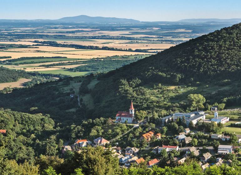 Panoramatický pohled na vesnici v údolí, obklopenou lesy a poli. Pozemky vhodné k bydlení.