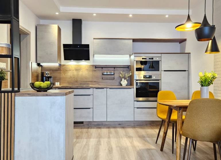 Kuchyně v 1-pokojovém bytě s podlahou s dřevěným dekorem, jídelní stůl a žluté židle.