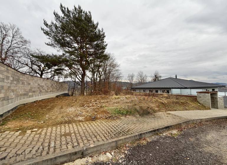 Pozemek na bydlení ve Velké Bytči ve městě Bytča s chodníkem a stromy.